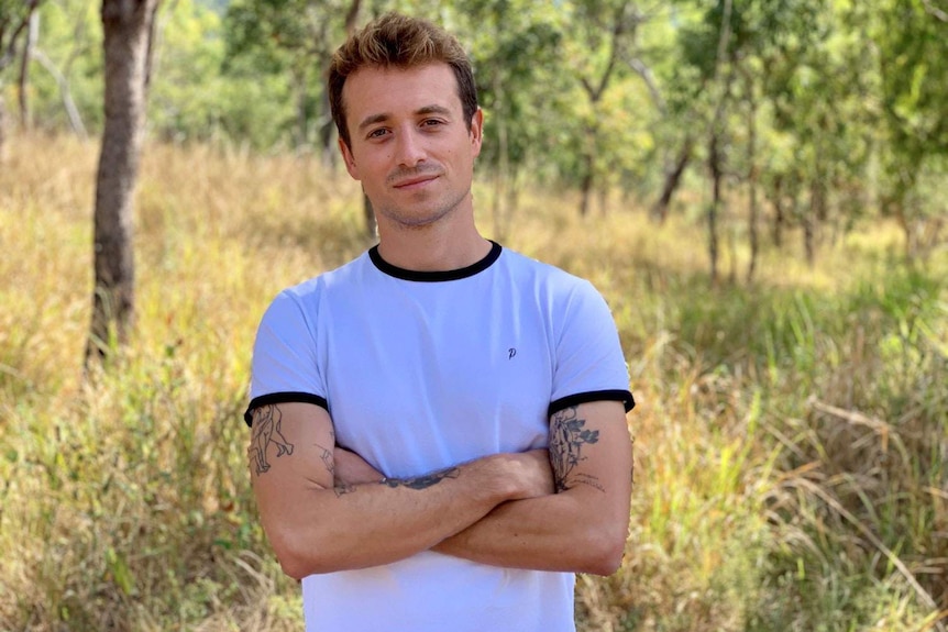 French journalist Hugo Clement stands with arms folded in front of trees.