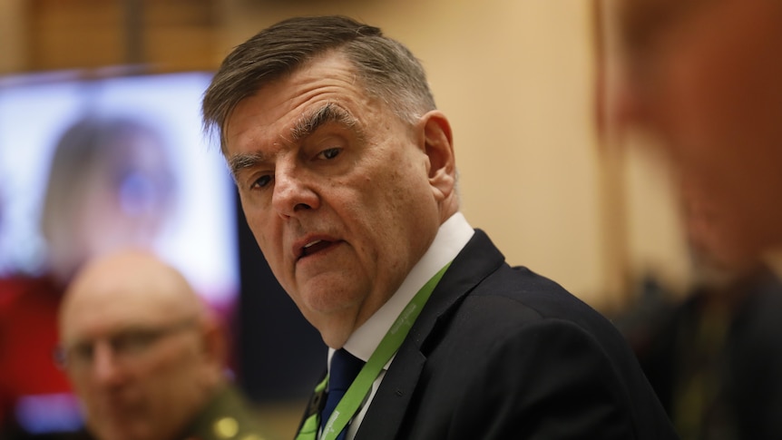 A man wearing a lanyard looks down inside a committee room.