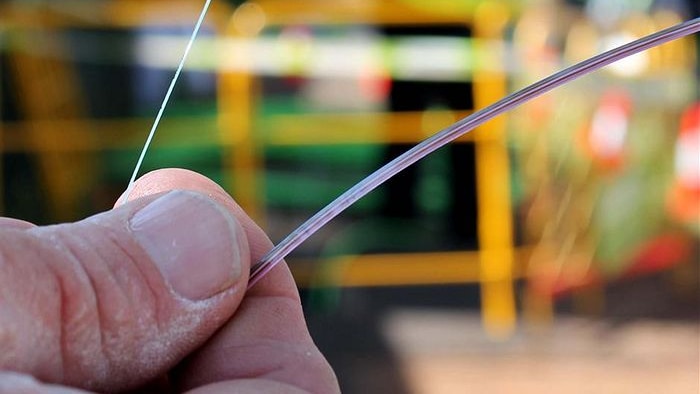 A person holding a piece of NBN fibre in between their fingers.