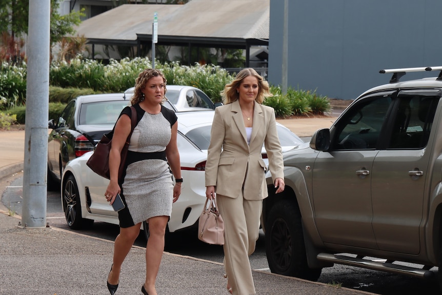 Two women walk along a street. They are both wearing corporate wear. 