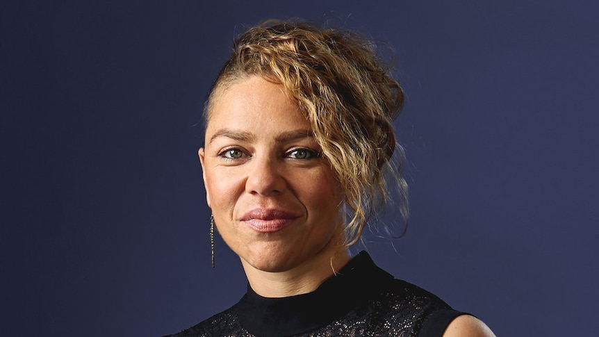 Veronique Serret stands in front of a blue background smiling at the camera