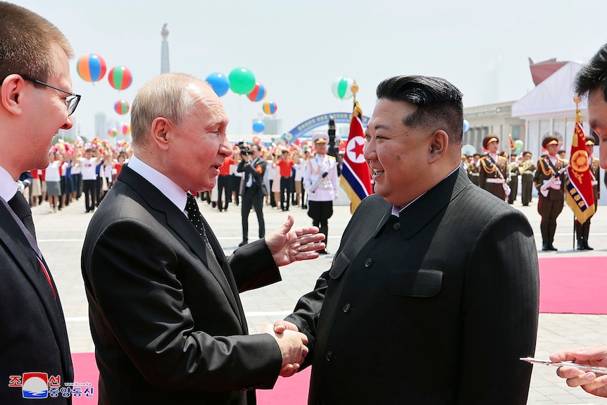 Vladimir Putin and Kim Jong Un shake hands.