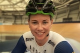 Young woman bends over her bike smiling in Olympic racing uniform at velodrome.