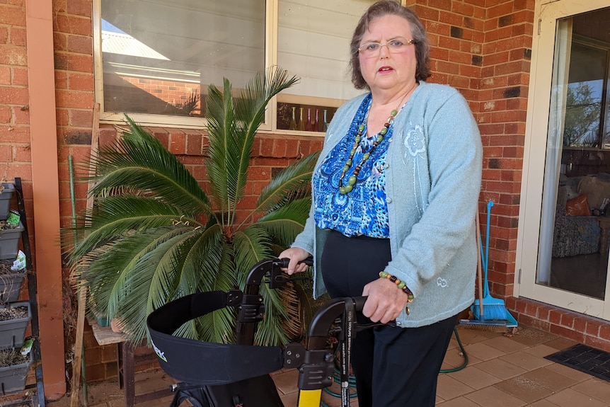 An older woman standing with her walker outside her home.