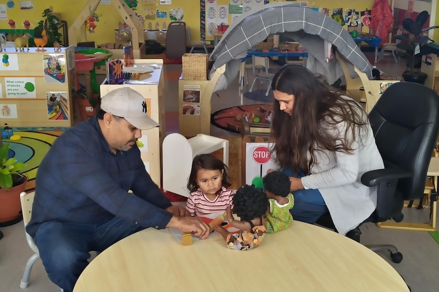 Brian and Shirleen playing with their daughter on a low wooden table.