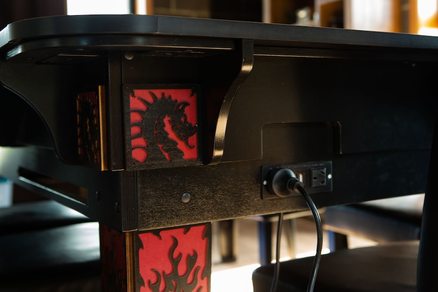 A large games table with red and black dragon motifs and USB and power ports built in.