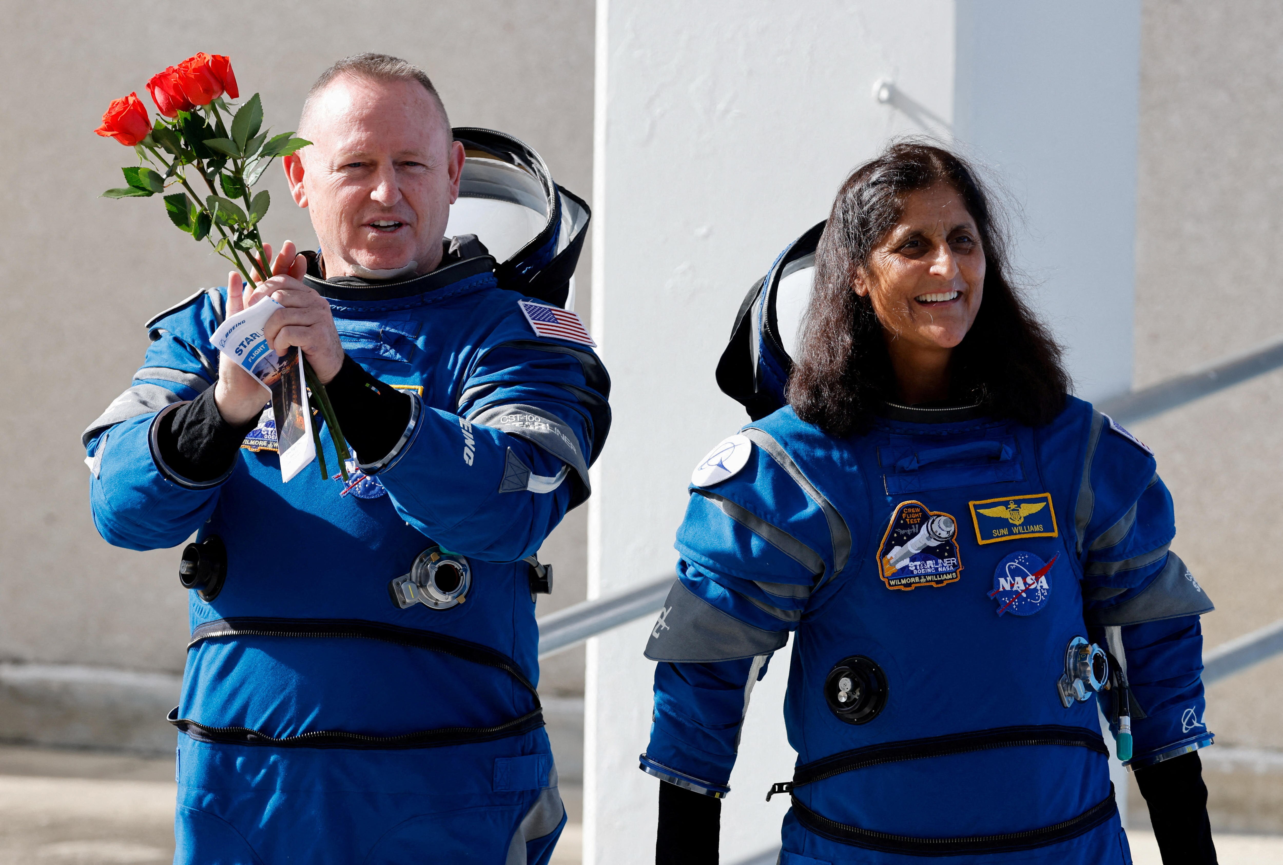 A white man and south-east Asian woman grin as they wear blue spacesuits