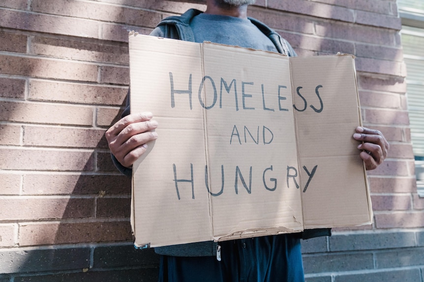 A homeless person with a sign that says they are hungry and need help.