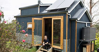 A woman sits no the steps of a small house.