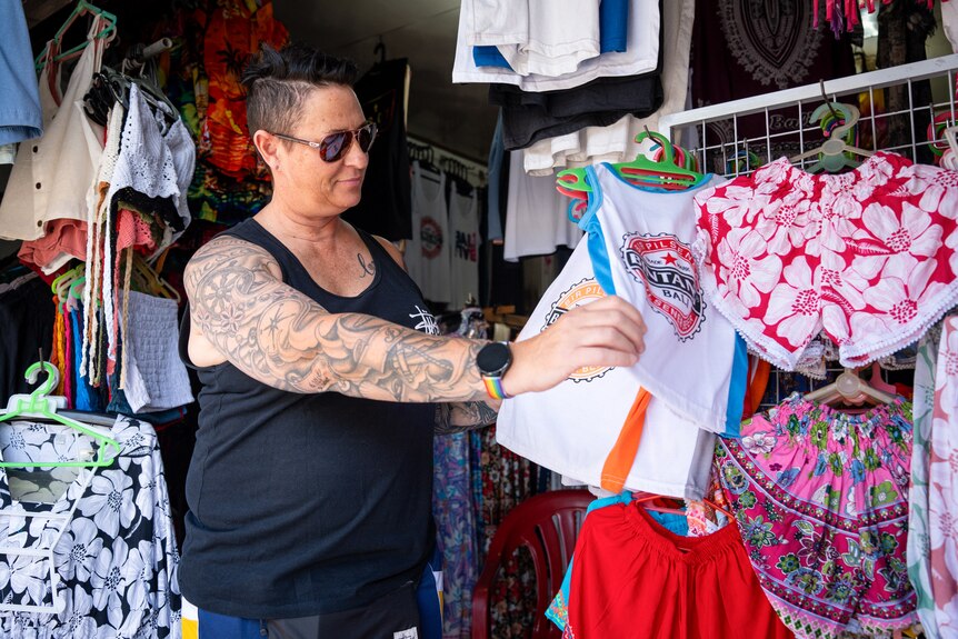 A woman with a tattoo on her arm and wearing sunglasses looks at t-shirts in Bali.