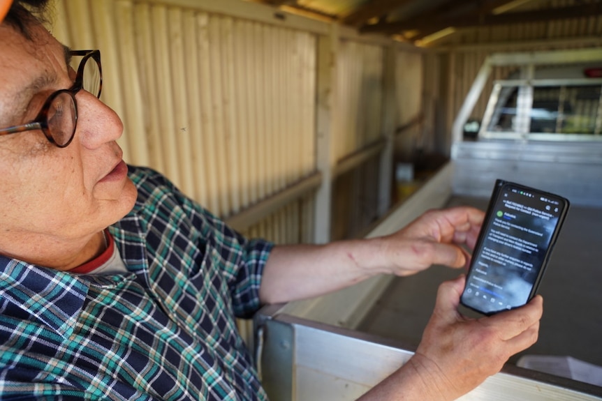 A bespectacled older man wearing a cap operates his phone.