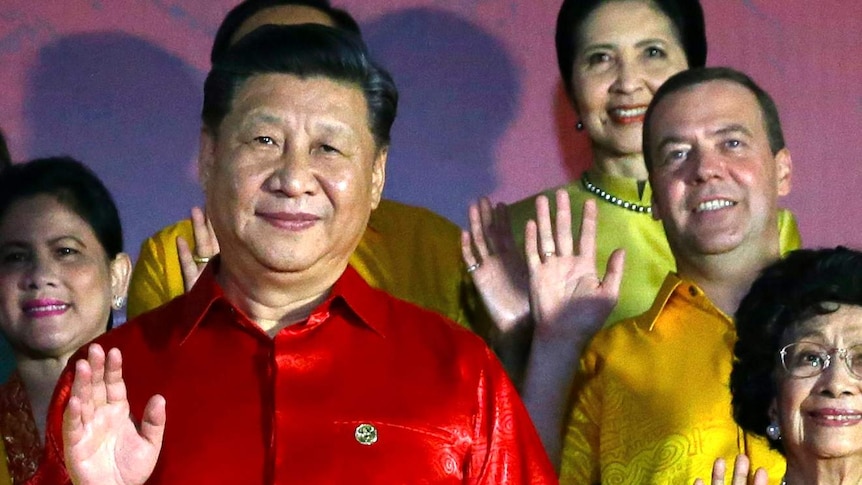 Chinese President Xi Jinping waves at the camera, wearing a red silk shirt, with other leaders similarly dressed