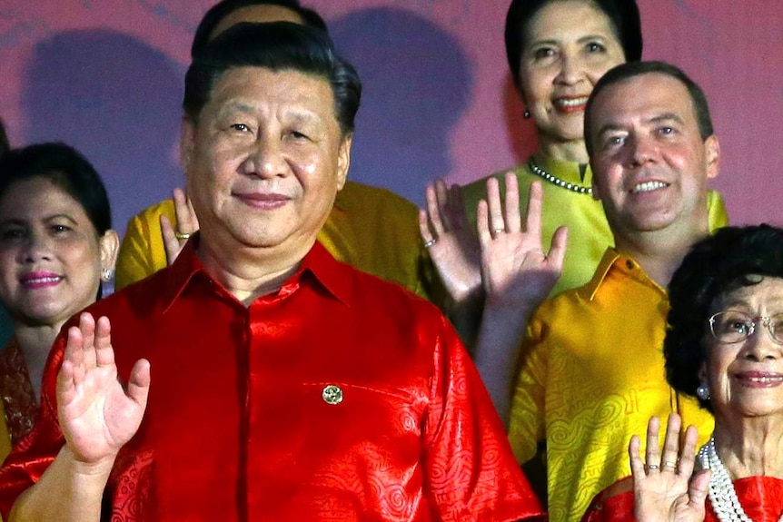 Chinese President Xi Jinping waves at the camera, wearing a red silk shirt, with other leaders similarly dressed