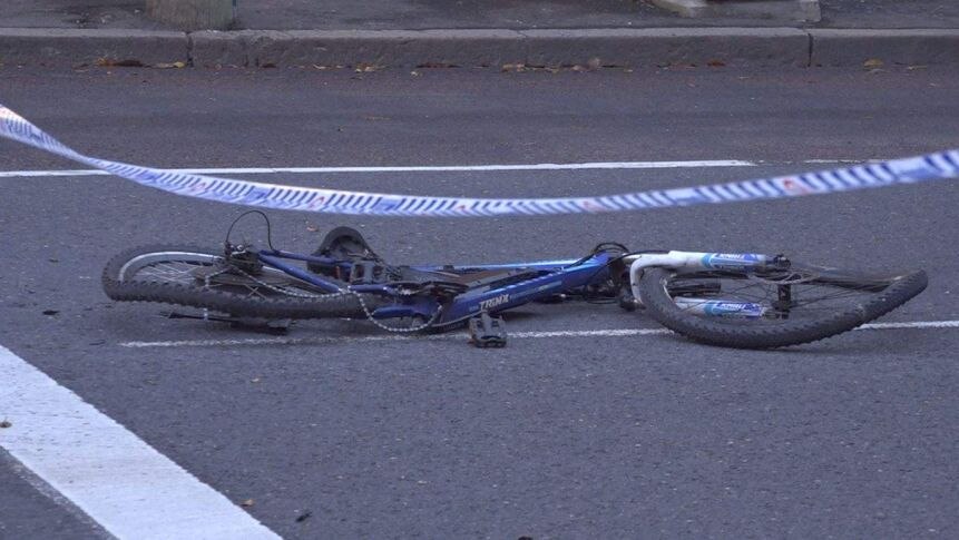 A bent bike lies in the middle of the road, blocked off by police tape.