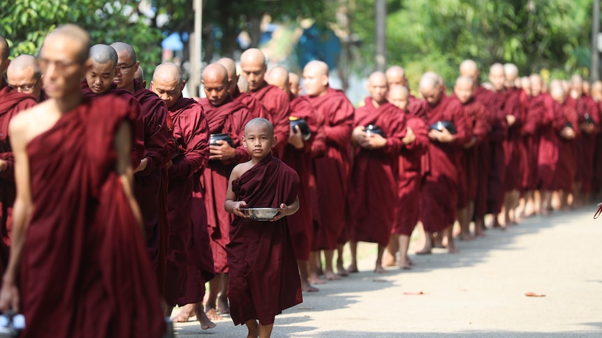 Buddhist monks in red robes walk to collect their morning alms from devotees 