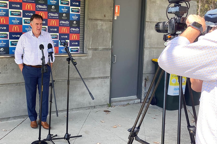 A man stands in front of journalists and cameras and microphones