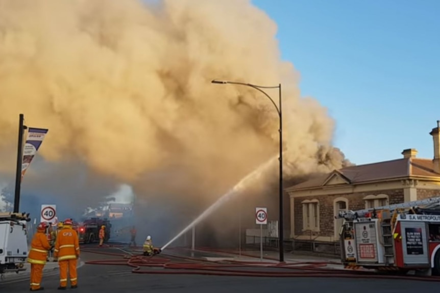 Two CFS volunteers stand beside a fire truck, as large plumes of smoke rise into the air from a building fire