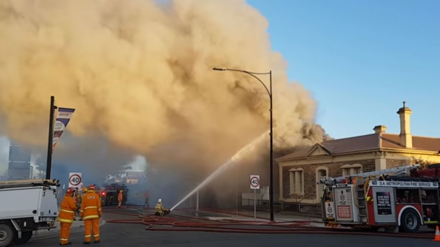 Two CFS volunteers stand beside a fire truck, as large plumes of smoke rise into the air from a building fire