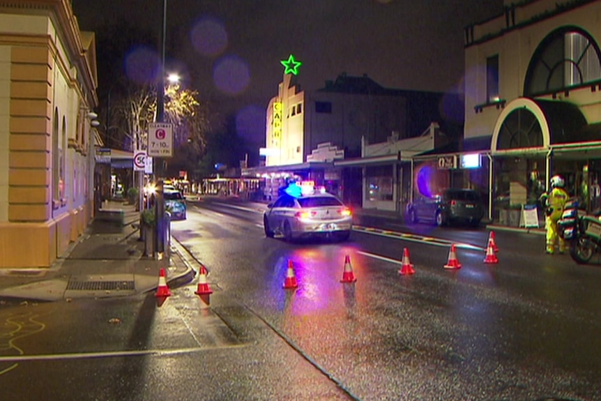 A police car in the middle of a wide wet road at night with buildings behind