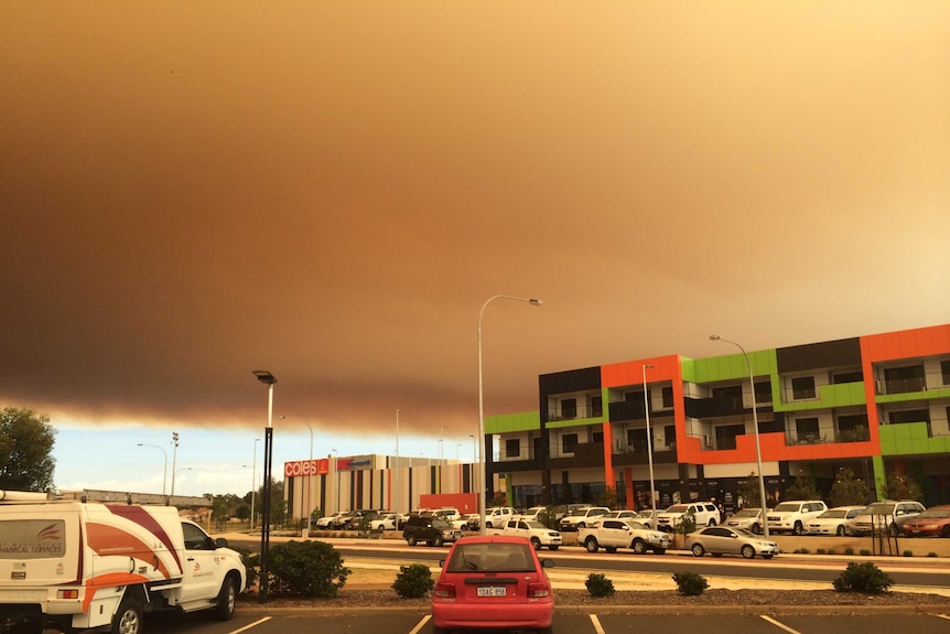 A large bank of bushfire smoke in the distance makes its way across the sky over the top of buildings in the foreground.