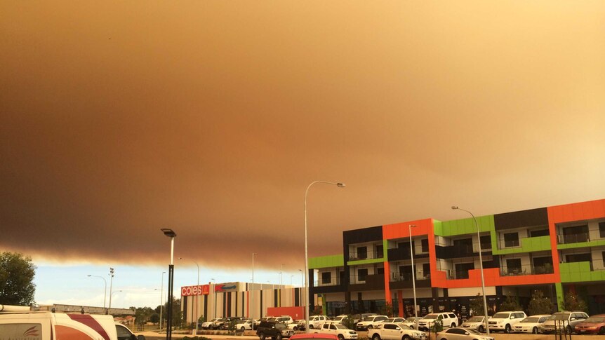 A large bank of bushfire smoke in the distance makes its way across the sky over the top of buildings in the foreground.