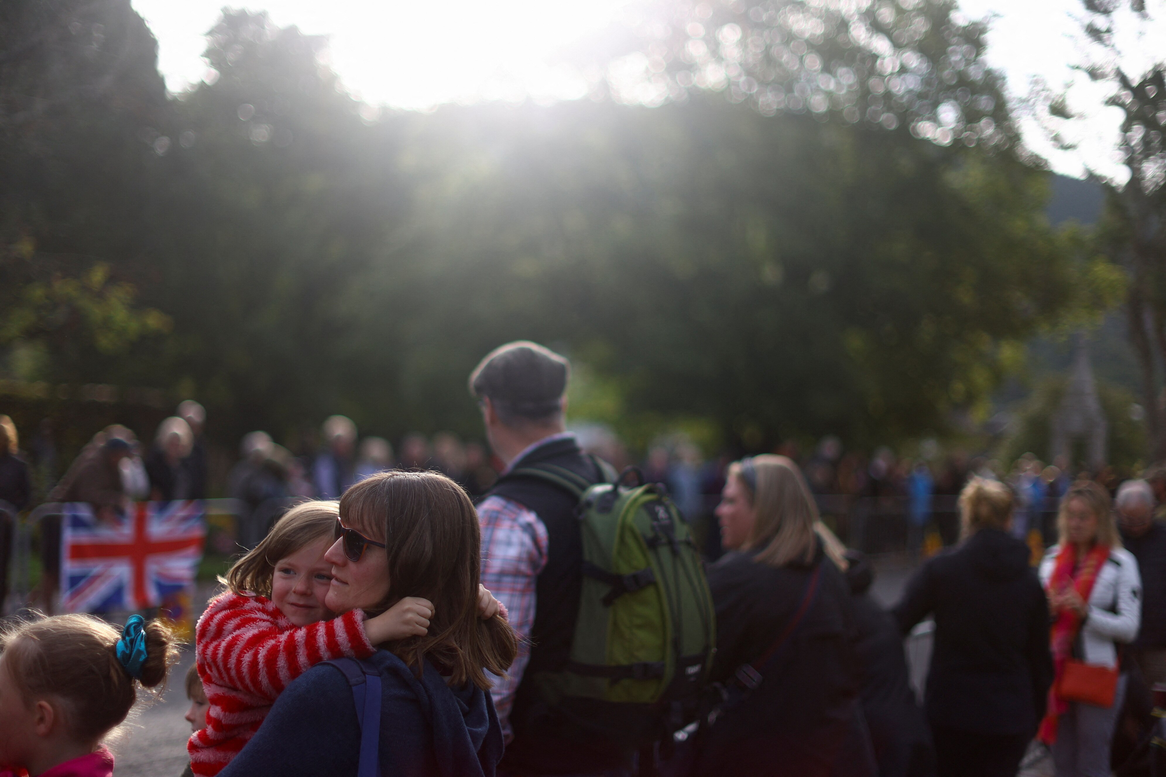 A woman holds her daughter among crowds lining a road in the Scottish countryside. 