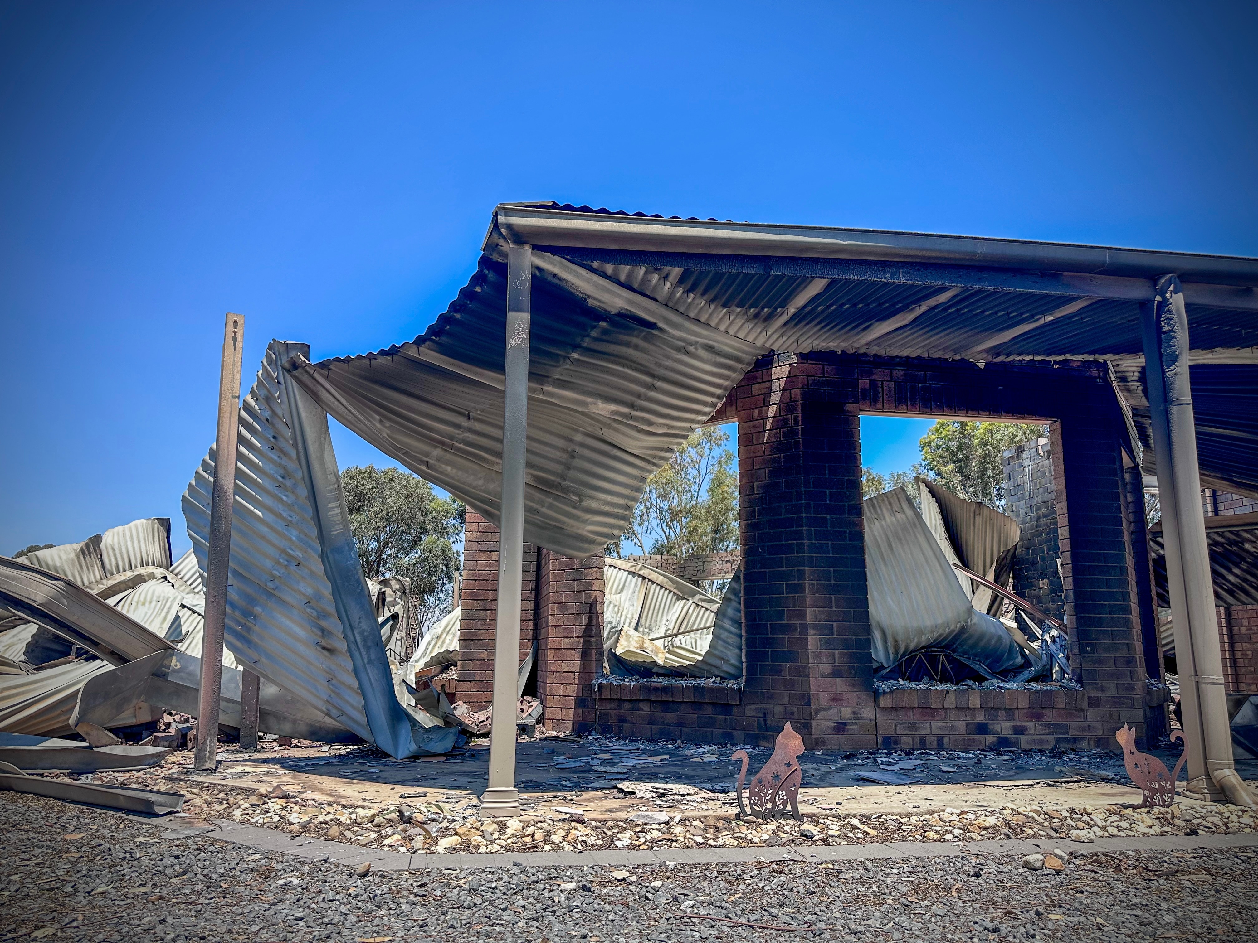 Techo derrumbado en casa ennegrecida, pequeñas esculturas de gatos permanecen en el suelo.