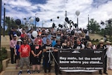 A large group of people gathers on the steps near the Mildura Riverfront, some are holding balloons and other carry a sign