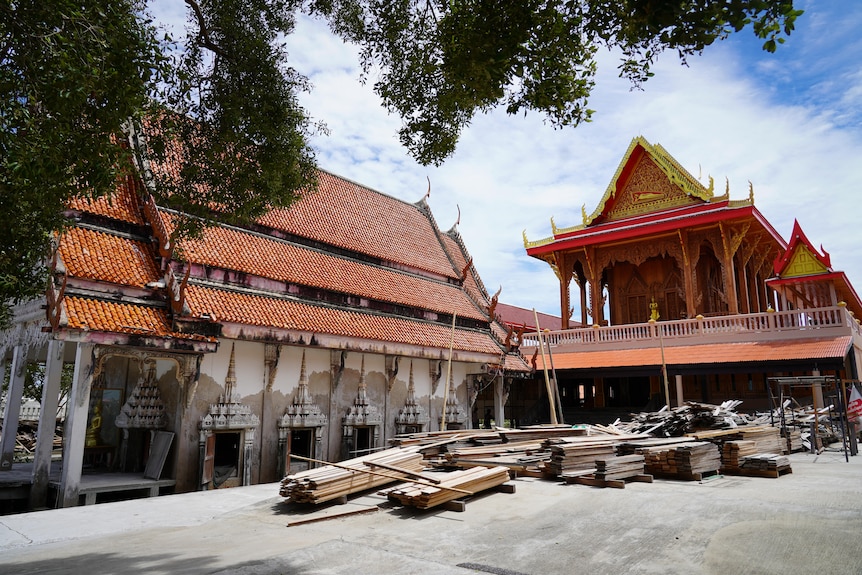 Piles of timber and other building supplies sit in a paved courtyard next to ornate temple buildings
