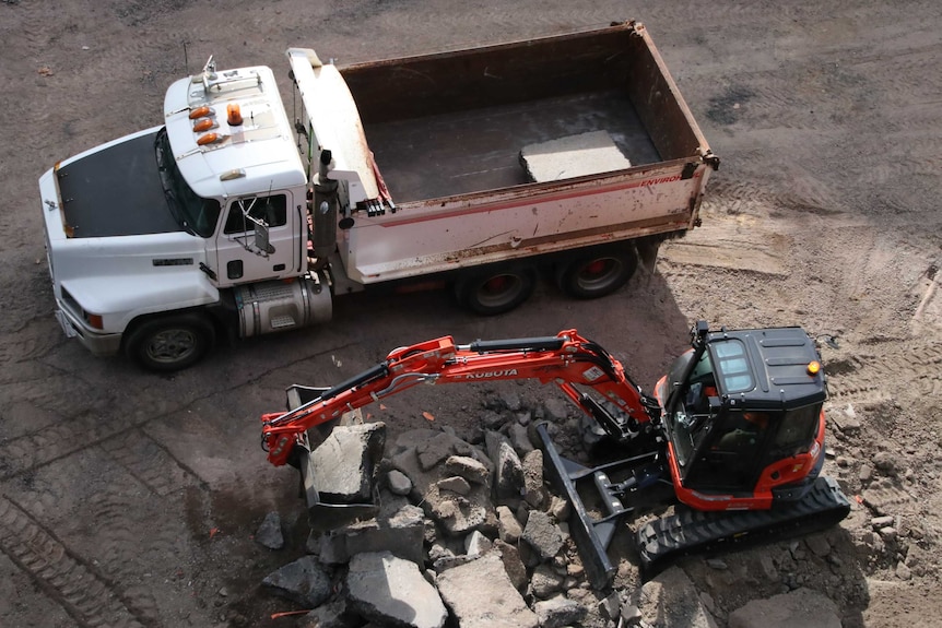 Looking down on a dump truck and a digger which is next to a pile of broken concrete.