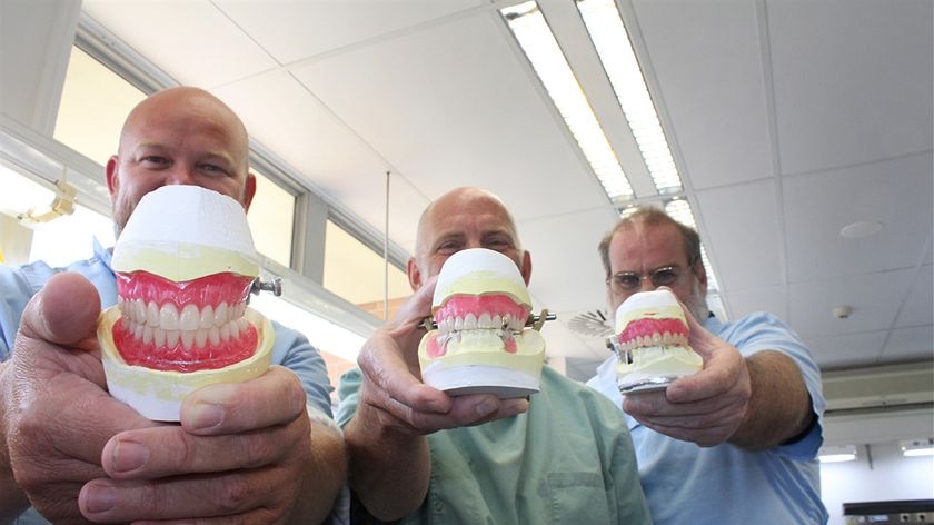 Three men holding sets of dentures