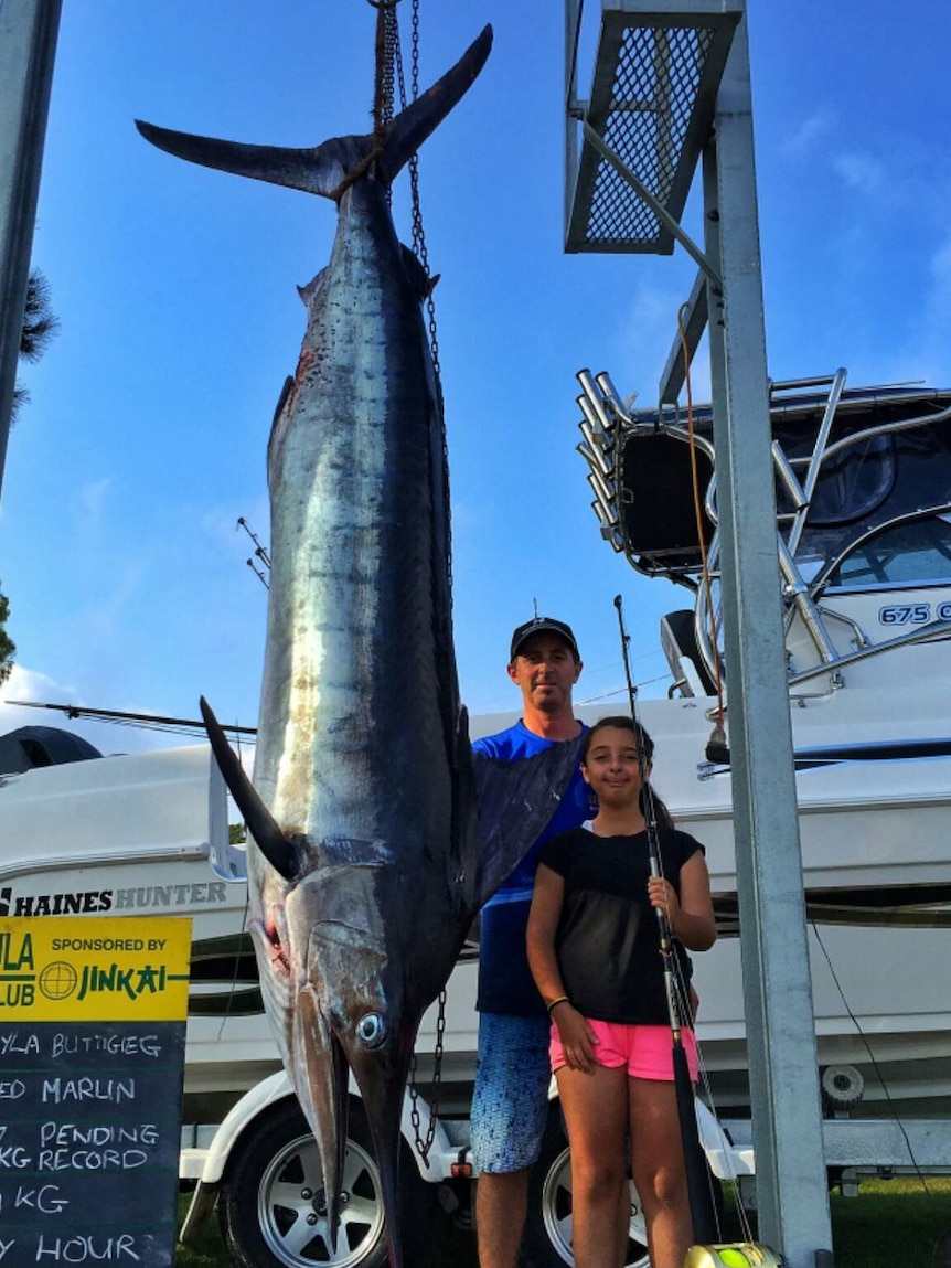 Girl poses next to huge fish and her dad
