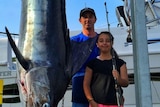 Girl poses next to huge fish and her dad