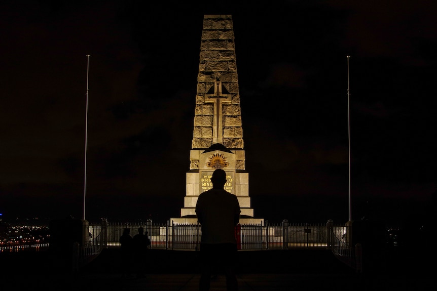 A silhouette of a man as he looks up at a memorial which is lit up in pitch darkness