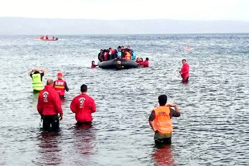 Volunteer lifesavers walk out to help a boat full of refugees in Lesbos