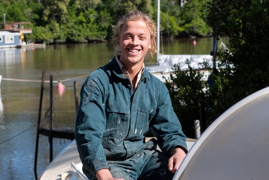 Un jeune homme assis sur la barque qu'il a construite.