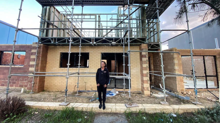 A woman stands in front of a house that is under construction.