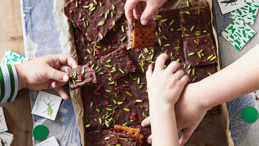 Kids hands reaching for salted caramel crack slice in tray on tablecloth.