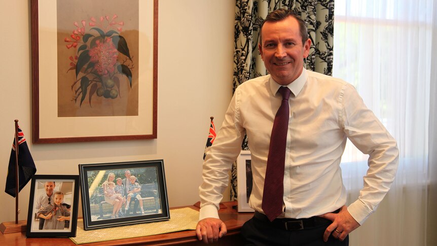 WA Premier Mark McGowan standing in front of a table displaying framed photos of his family.
