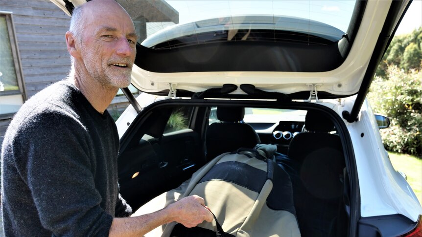 A man loads a double bass into the back of his white electric vehicle.