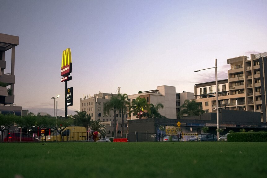 A public park at dusk, beyond it are buildings and a McDonalds.