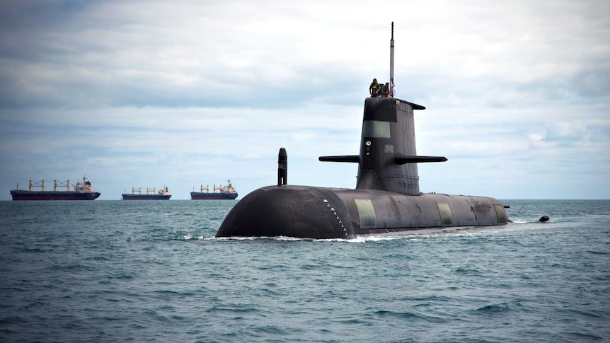 A submarine with some people on top and some ships in the distance behind