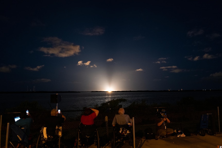 People on chairs watching a rocket launch.