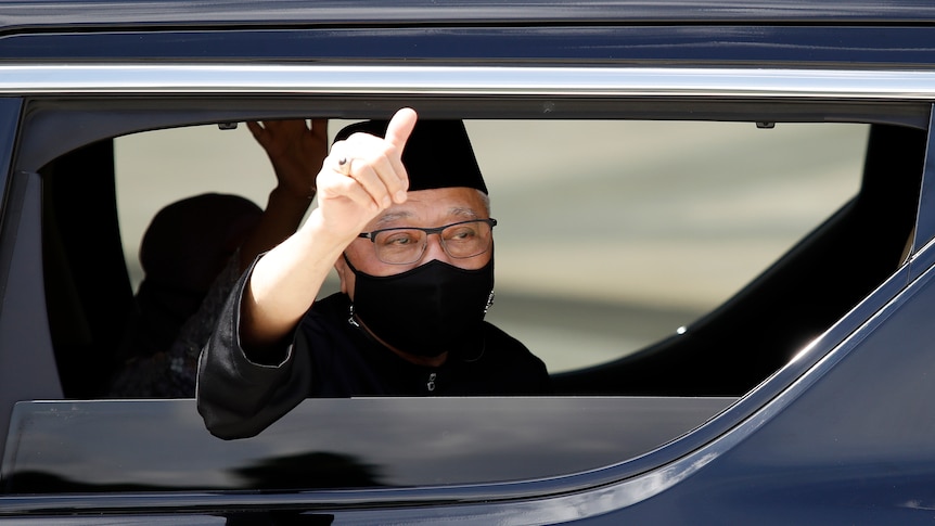 The newly sworn in Malaysian PM waves from inside his car as his car as he leaves the National Palace in Kuala Lumpur