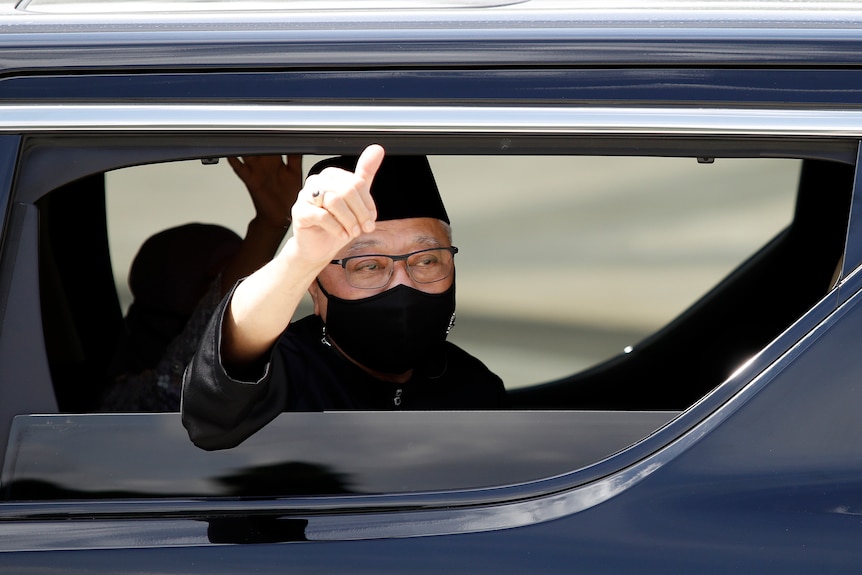 The newly sworn in Malaysian PM waves from inside his car as his car as he leaves the National Palace in Kuala Lumpur