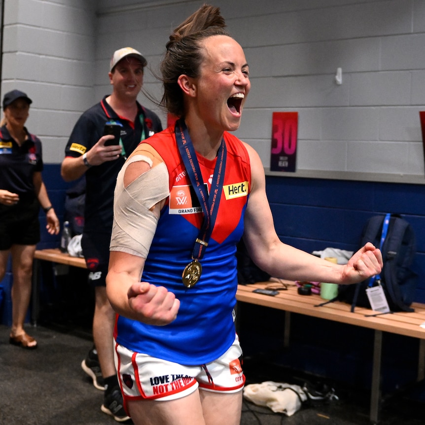 Daisy Pearce pumps her fists and yells in delight while wearing her premiership medal in the Demons changerooms