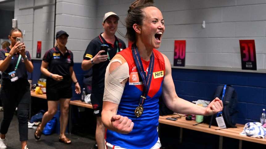 Daisy Pearce pumps her fists and yells in delight while wearing her premiership medal in the Demons changerooms