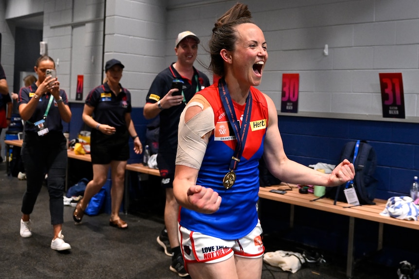 Daisy Pearce pumps her fists and yells in delight while wearing her premiership medal in the Demons changerooms