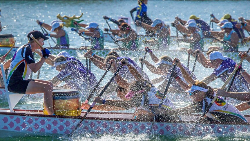 Three dragon boats are paddling neck to neck during a race