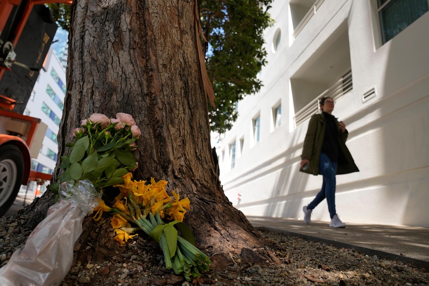 A woman walks past flowers left outside an apartment building